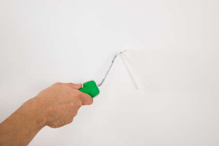 Young man using paint roller on white wall at homeの写真素材