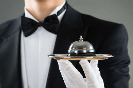 Midsection of waiter holding service bell in plate against gray background