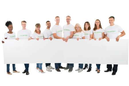 Full length portrait of confident volunteers holding blank billboard against white backgroundの写真素材