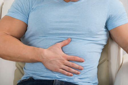 Midsection of man with stomach ache sitting on couch at homeの写真素材