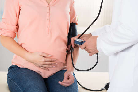 Midsection of male doctor checking pregnant woman's blood pressure in hospital