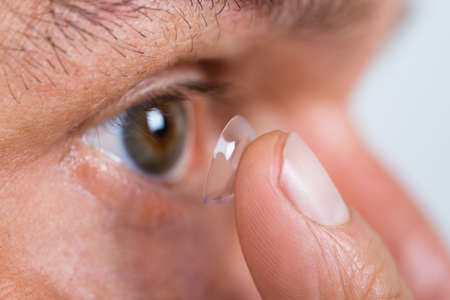 Closeup of man putting contact lens in eye over white backgroundの写真素材