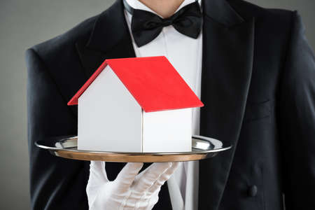 Midsection of young waiter holding house model in tray against gray backgroundの写真素材