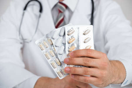 Midsection of doctor holding blister packs against white backgroundの写真素材