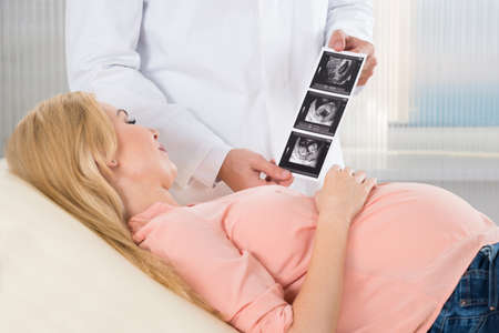 Midsection of doctor showing ultrasound scan to pregnant woman in hospital