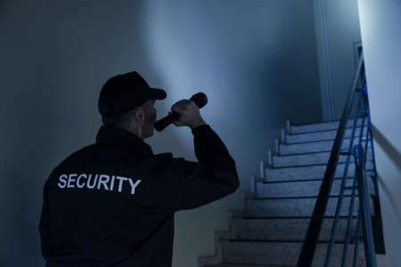 Rear view of security guard searching on stairway with flashlight in office building