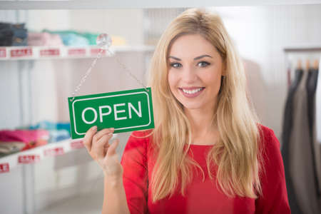 Portrait of confident female owner holding open sign in clothing store