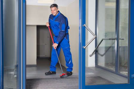 Full length portrait of confident mature worker with broom cleaning floorの写真素材