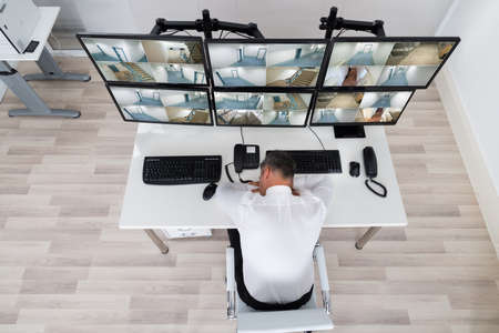 High angle view of operator sleeping while leaning on security monitor's desk in office