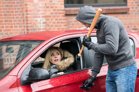 Male robber holding baseball bat while looking at scared woman in car