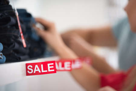 Closeup of sale sign on shelf with couple in background at clothing store