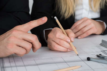 Cropped image of young engineers discussing over blueprint at desk in office