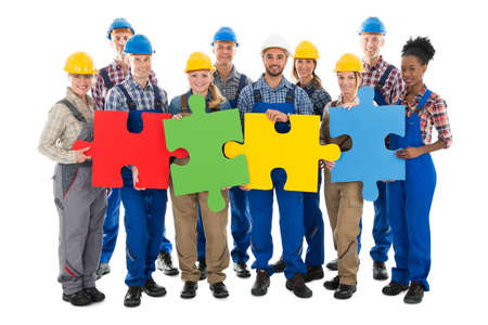 Portrait of confident construction workers joining jigsaw pieces against white backgroundの写真素材