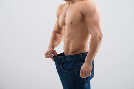 Midsection of muscular man in old jeans showing weight loss against white backgroundの写真素材