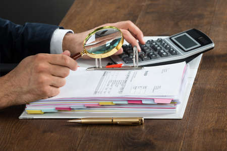 Cropped image of businessman checking invoice with magnifying glass at desk
