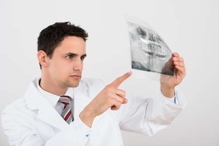Young male dentist examining dental xray against white backgroundの写真素材
