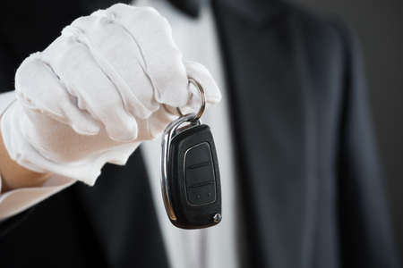 Midsection of waiter holding car key against gray backgroundの写真素材