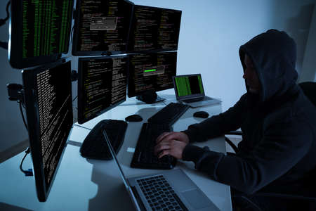 Rear view of hacker using computers to steal data in office
