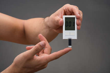 Cropped hands of man checking blood sugar level with glucometer against gray backgroundの写真素材