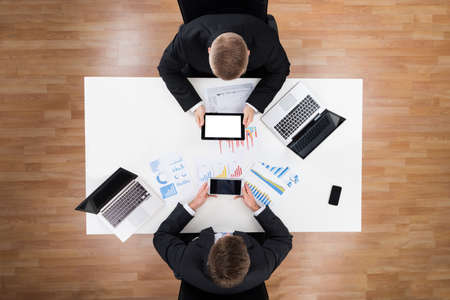 Directly above shot of businessmen using technologies with financial charts on table