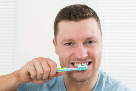 Closeup of mid adult man brushing teeth at homeの写真素材