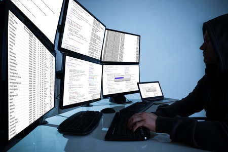 Side view of hacker using computers to steal data in office