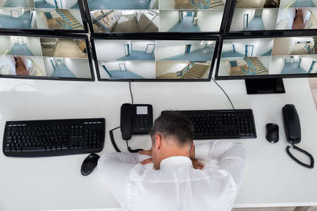 High angle view of operator sleeping while leaning on security monitor's desk in office
