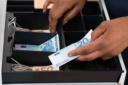 Close-up Of Person's Hand Holding Euro Note Over Container