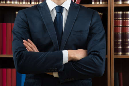 Midsection of male lawyer standing against bookshelf in courtroom
