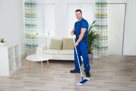 Full length portrait of smiling worker cleaning floor with mop at home