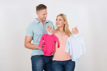 Smiling couple looking at each other while holding baby clothing over white backgroundの写真素材