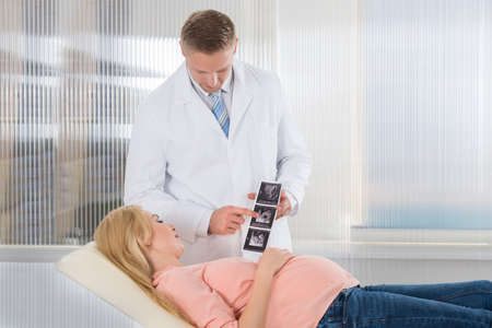 Young doctor showing ultrasound scan to pregnant woman in hospital