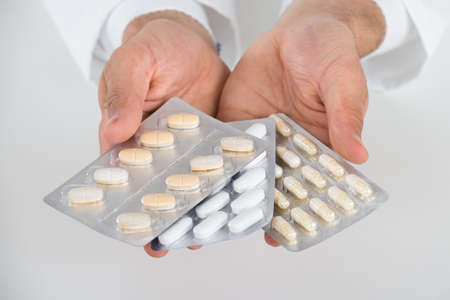 Cropped hands of doctor holding blister packs against white background