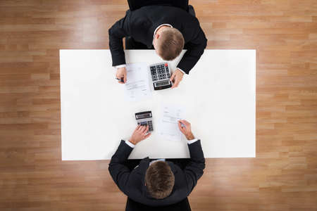 Directly above shot of businessmen using calculators at desk in office
