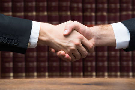 Cropped image of judge and client shaking hands against books at courtroomの写真素材