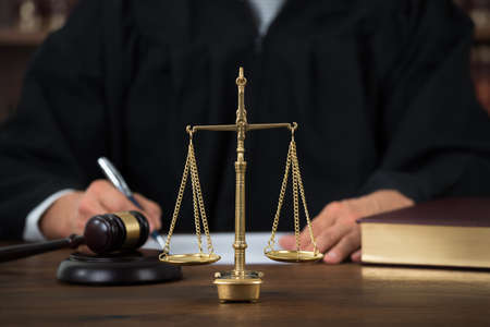 Law scales on table with judge writing in background at courtroom
