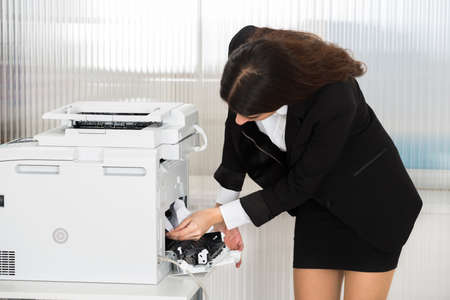 Young businesswoman removing paper stuck in printer at office