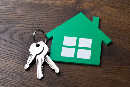 High angle view of green paper house and keys on wooden table