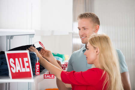 Young couple looking at sale tag on jeans at clothing store