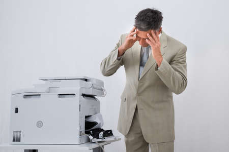 Irritated businessman looking at paper stuck in printer at office