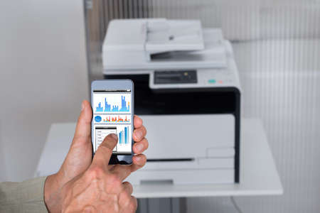 Cropped image of businessman giving print command on smart phone in officeの写真素材