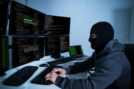 Male hacker using computers with multiple monitors to hack