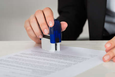 Cropped image of young businesswoman stamping contract document at office desk