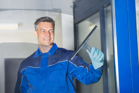 Happy mature male worker cleaning glass with squeegee