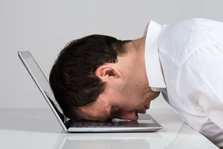 Side view of stressed businessman leaning on laptop at desk against white background