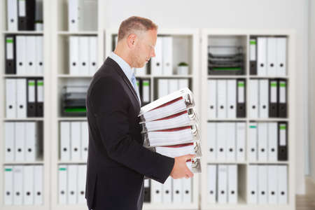 Side view of mid adult businessman carrying binders in office