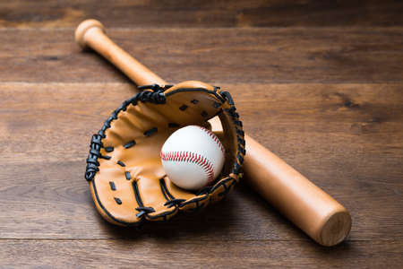 High angle view of baseball glove and ball with bat on wooden tableの写真素材