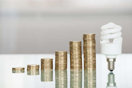 Close-up Of Fluorescent Light Bulb And Stacked Coins On Desk