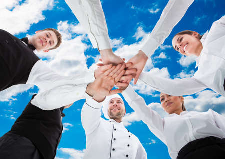 Low angle view of waiters and waitresses stacking hands against sky
