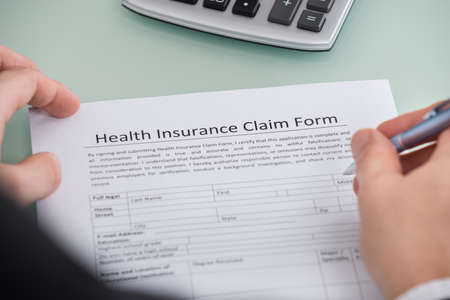 Close-up Of Person Filling Health Insurance Claim Formの写真素材